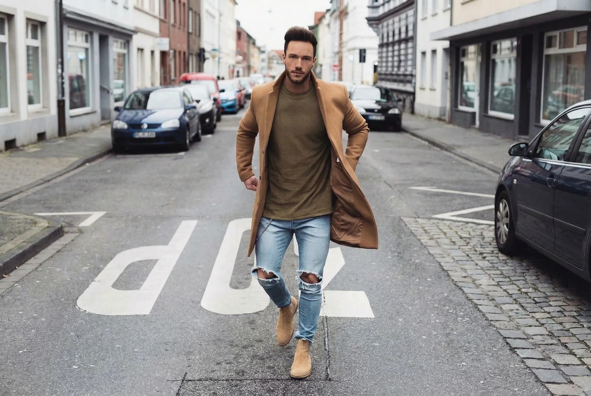 Stylish man in camel coat and ripped jeans crossing zebra crossing on European city street