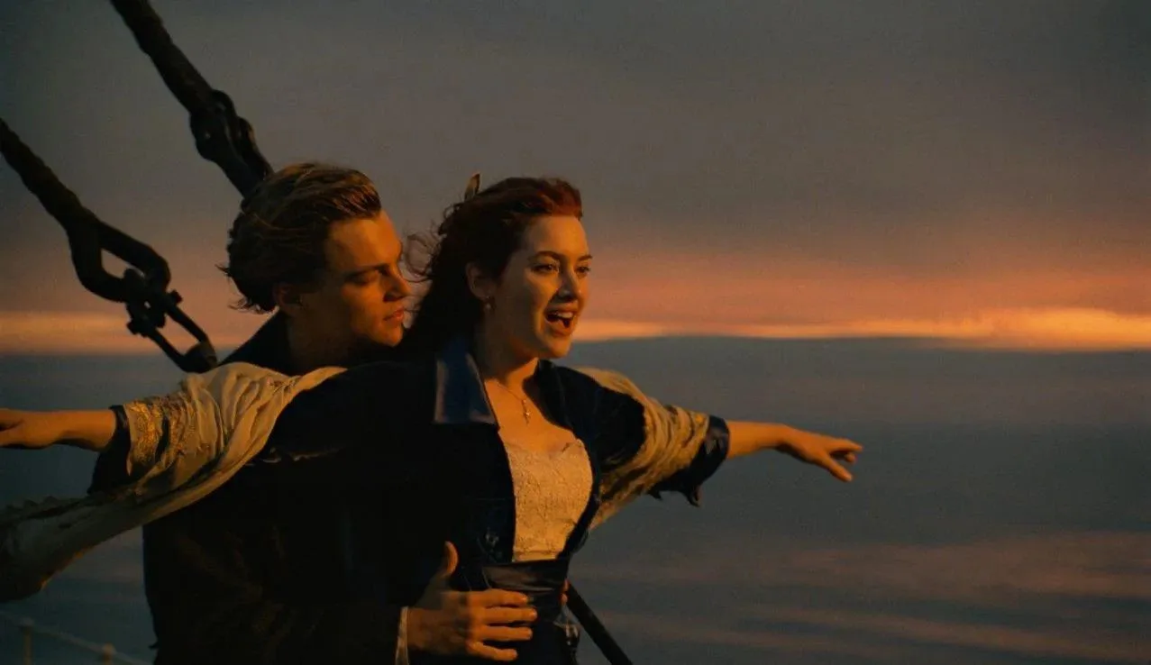Couple standing at ship bow with arms outstretched against ocean sunset, iconic romantic scene on maritime vessel
