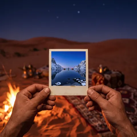Two hands by a desert campfire hold up a print of a snowy fjord